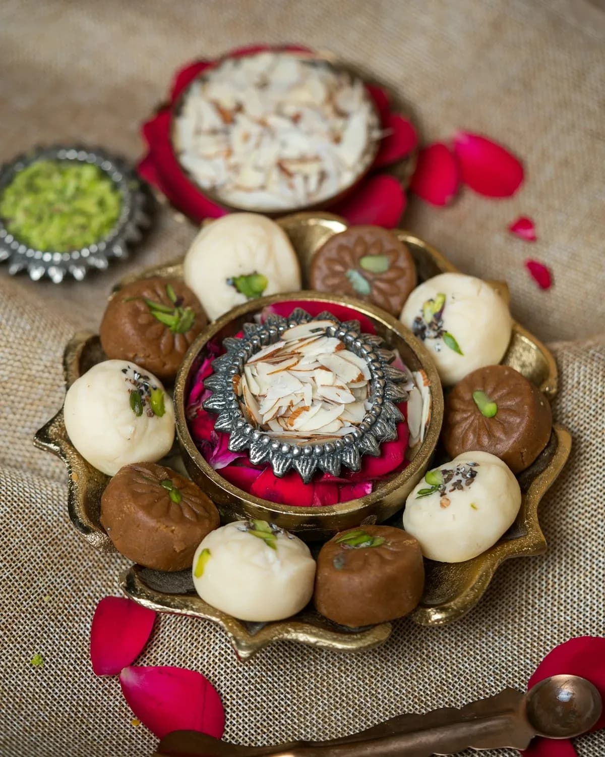 Brass platter of kesar and chocolate peda with sliced almonds, pistachios and rose petals